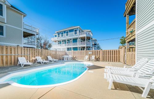 a backyard with a pool and chairs and a house at On Island Time in Kill Devil Hills