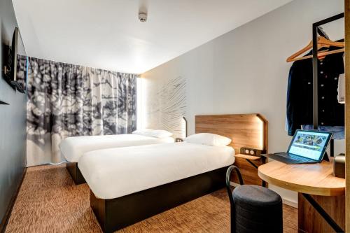 two beds in a room with a desk and a laptop at B&B HOTEL Paris Ivry Quai de Seine in Ivry-sur-Seine