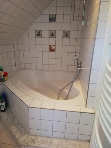 a bath tub with a shower in a white tiled bathroom at Ferienhaus Königs Wusterhausen in Königs Wusterhausen