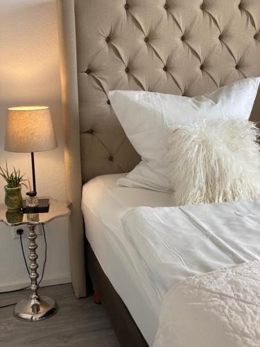una cama con sábanas blancas y una lámpara sobre una mesa en Aurum Apartment, en Kirchheim am Neckar