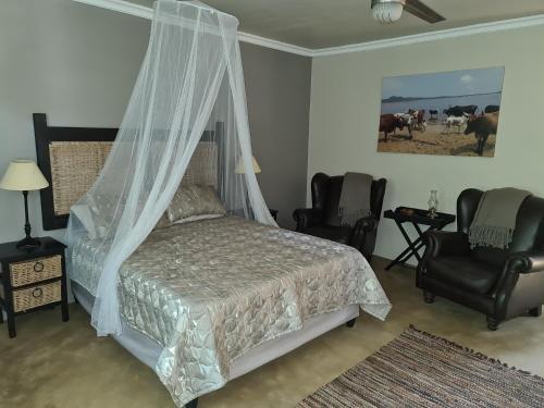 a bedroom with a bed with a canopy and two chairs at Kosi Bay Lake House in KwaMazambane