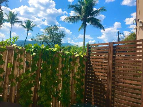 a fence with a palm tree in the background at Casa d'Aroeira Residencial Boutique - Centro de Juqueí - 2 quadras do mar - Serviço de Praia - Roupa de Cama 600 fios algodão Egípcio - Toalhas Banho e Praia - Tudo Novo - Estacionamento Interno - Cozinha - Consulte unidades com Ofurô Hidro e Cromoterapia in Juquei