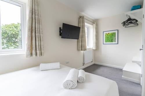 a white bedroom with a bed and a tv at The Woodland Collection, 10 mins from beaches in Hayle