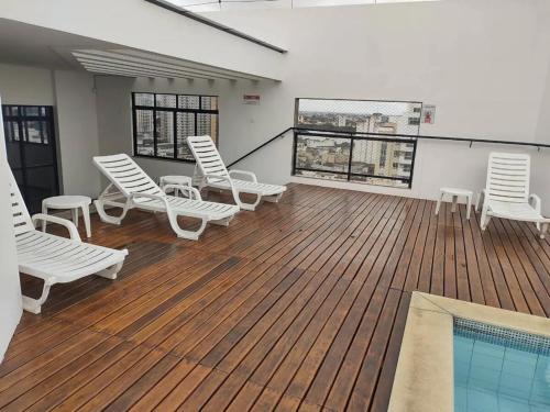 a deck with white chairs and a swimming pool at Apto acolhedor, confortável e bem localizado in Campos dos Goytacazes