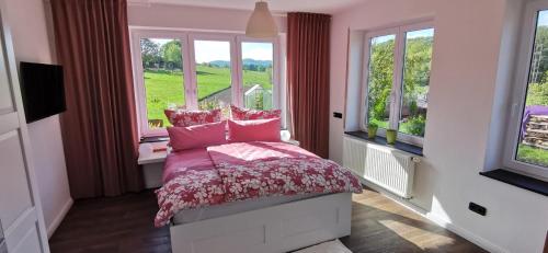 um quarto com uma cama com lençóis cor-de-rosa e janelas em Ferienwohnung Rhön Natur em Hilders