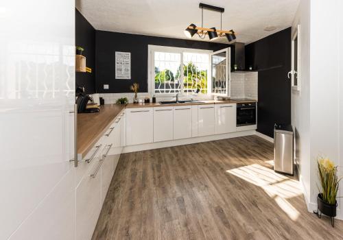 a kitchen with white cabinets and black walls and wood floors at Villa des palmiers - Magnifique villa avec piscine privée et chauffée selon saison in Bon-Encontre