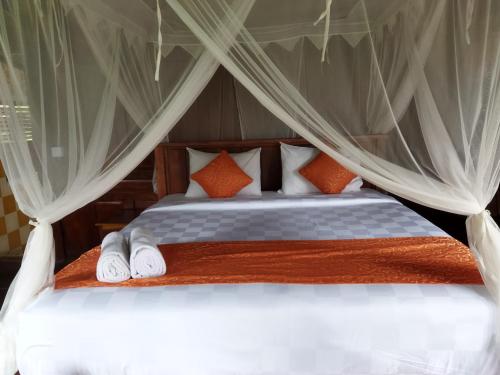 a bedroom with a canopy bed with white sheets and orange pillows at D'Ume Bendoel Homestay in Jatiluwih