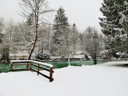 a park bench covered in snow next to a pond at Apartma M&J in Mojstrana