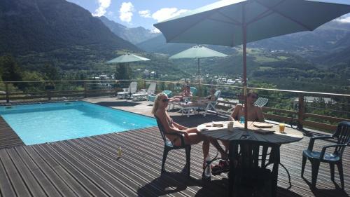 a man and woman sitting at a table next to a pool at Chalet les Moineaux Chambres d'Hôtes in Jausiers