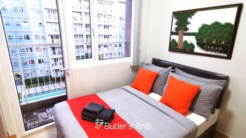 a bedroom with a bed with orange pillows and a window at Butler's BnB @ Trees Residences QC Phil in Manila