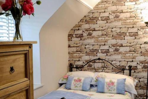 1 dormitorio con pared de piedra y 1 cama con almohadas en Woodbank Cottage Newton Stewart, en Newton Stewart