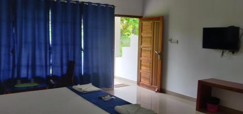 a bedroom with a bed with blue curtains and a television at Hotel Exotica Squares in Neil Island