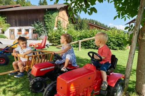 three children riding on toy tractors in a yard at Apartments Untersüßgut Eben in Eben im Pongau