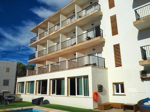 a white building with a balcony and a swimming pool at Hotel Rocamar in Cala Figuera
