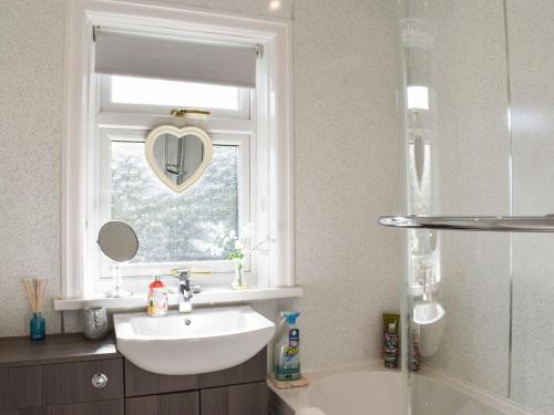 baño con lavabo y ventana con espejo en forma de corazón. en Holme Valley Cottage, en Holmfirth
