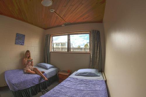 Centabay Lodge and Backpackers في بيهْيا: امرأة جالسة على سرير في غرفة بسريرين