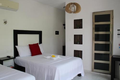 a bedroom with two beds with white sheets and red pillows at Casa Zazil in Bacalar