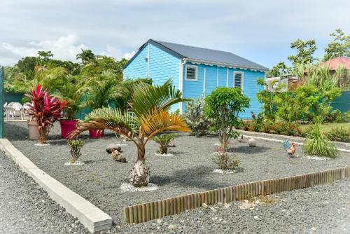 a blue house with palm trees and other plants at Les jardins de CHANTILLY -Bungalows 4 étoiles avec jardins et piscines privées in Baie-Mahault