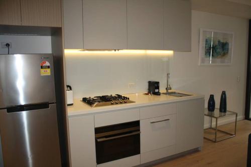 a kitchen with white cabinets and a stainless steel refrigerator at Large One Bedroom with Study-ALB09203 in Sydney