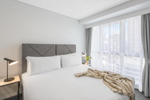 a bedroom with a white bed and a large window at Meriton Suites Adelaide Street, Brisbane in Brisbane