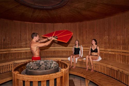 three people sitting in a sauna with a man holding an umbrella at Herning City Hotel in Herning