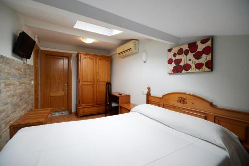 - une chambre avec un lit blanc et une télévision dans l'établissement Pensión Serafín, à Avilés