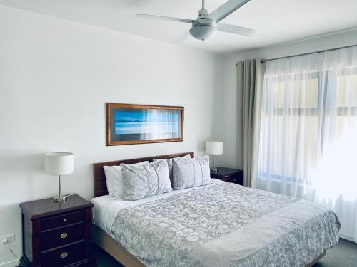 a white bedroom with a bed and a ceiling fan at Atlantic West Beach Apartments in Adelaide