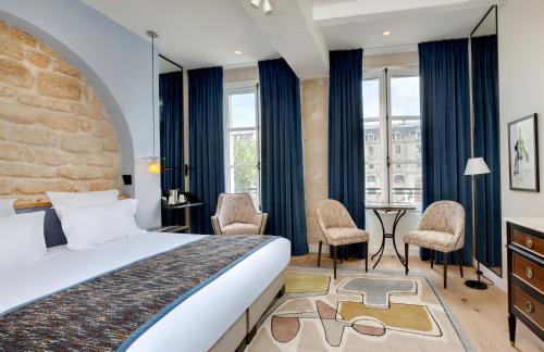 a hotel room with a bed and chairs and windows at Les Rives de Notre-Dame in Paris