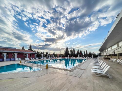 a large swimming pool with chairs and a cloudy sky at Spa Hotel Colossae Thermal in Pamukkale