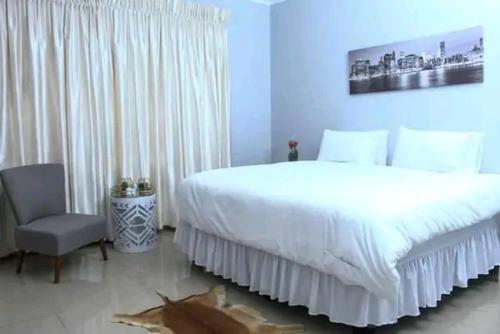 a bedroom with a large white bed and a chair at Luqa BnB in Empangeni