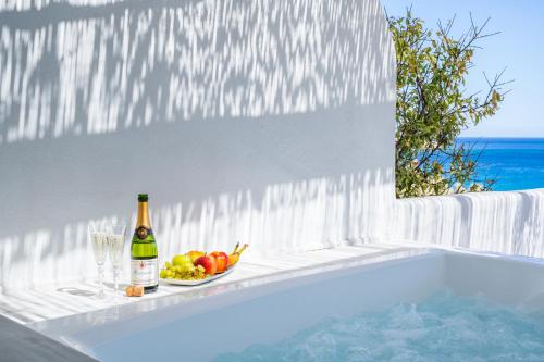 a bottle of wine and a bowl of fruit next to a bath tub at Poseidon Blue Gastronomy Hotel in Afiartis