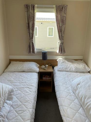 a bedroom with two beds and a window with curtains at Beautiful Butlins van in Lincolnshire