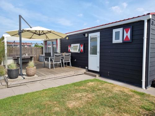a black house with a deck with a table and an umbrella at Chalet Serooskerke SE09 in Serooskerke