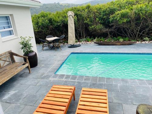 a swimming pool with two wooden chairs and a table at Mes Amis Beach Guest House in Wilderness