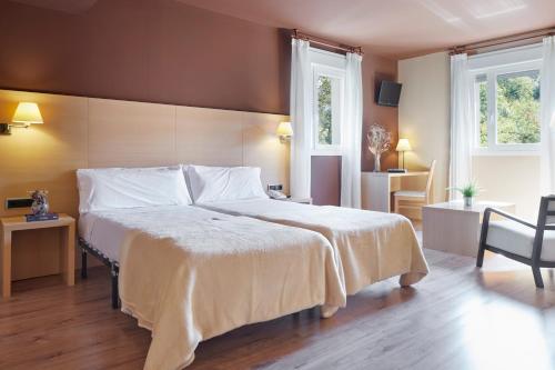a bedroom with a large bed and two windows at Iraipe Santuario de Arantzazu Hotel in Oñate