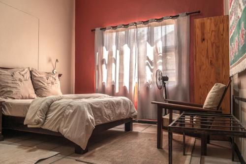 a bedroom with a bed and a chair and a window at Chameleon Backpackers & Guesthouse in Windhoek