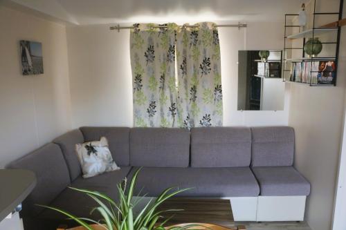 a living room with a gray couch in front of a window at Mobil-Home 3 chambres à "Les Mathes" in Les Mathes
