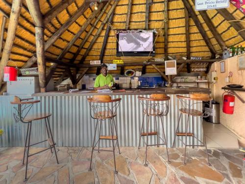 a woman standing behind a bar with stools at Chameleon Backpackers & Guesthouse in Windhoek