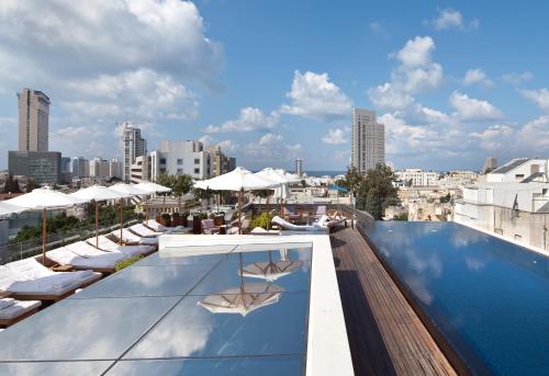 uma piscina no último piso com espreguiçadeiras e guarda-sóis num edifício em The Norman Tel Aviv em Tel Aviv