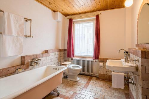 a bathroom with a tub and a toilet and a sink at Boutique Hotel Engadinerhof - A Home for Generations in Pontresina