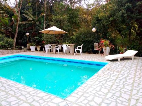 a swimming pool with a table and chairs and an umbrella at Chácara de Temporada - Mairiporã in Mairiporã