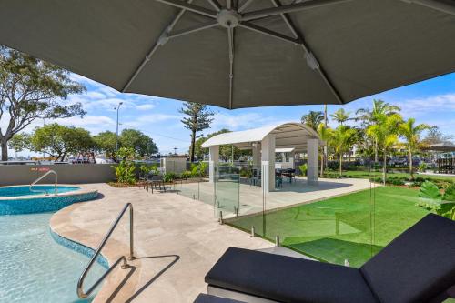 an outdoor pool with an umbrella and chairs and a table at Riverdance Apartments in Mooloolaba