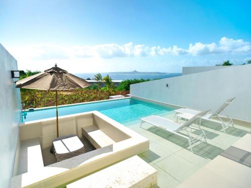 a swimming pool with two chairs and an umbrella at ADANRESORT LANA Villa Suite in Motobu