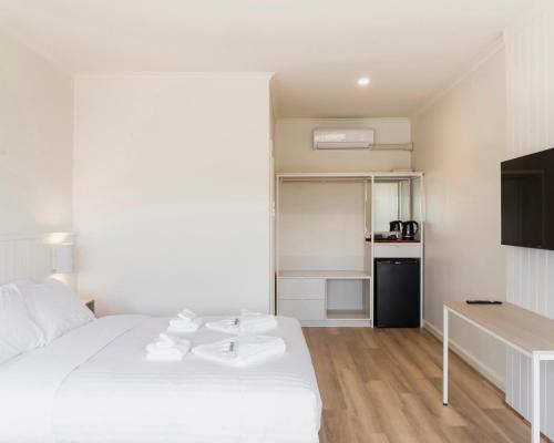 a bedroom with a white bed and a kitchen at Port Broughton Hotel and Sunnyside Motel in Port Broughton