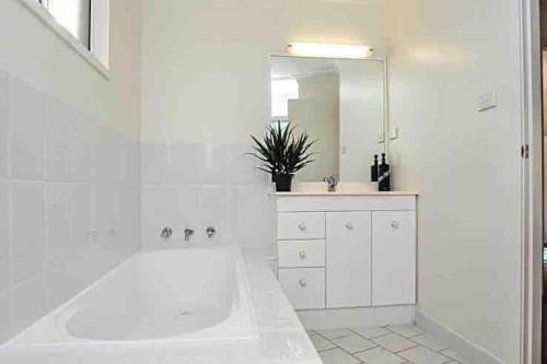 baño blanco con bañera y espejo grande en Beachfront Retreat - Ducted Air - Free Wifi, en Coffs Harbour