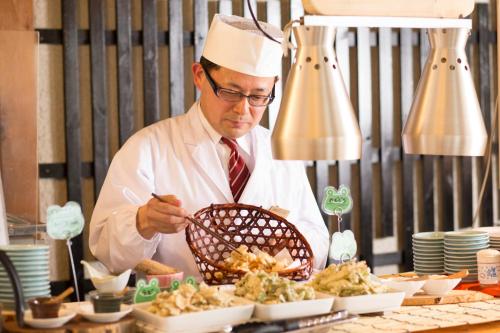 a man in a chefs hat preparing food at Hakuba Highland Hotel in Hakuba