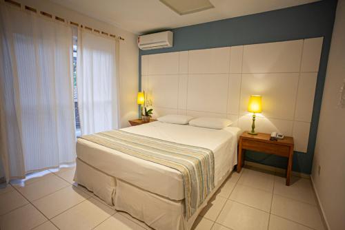 Un dormitorio con una gran cama blanca y una ventana en Juquehy Praia Hotel en Juquei