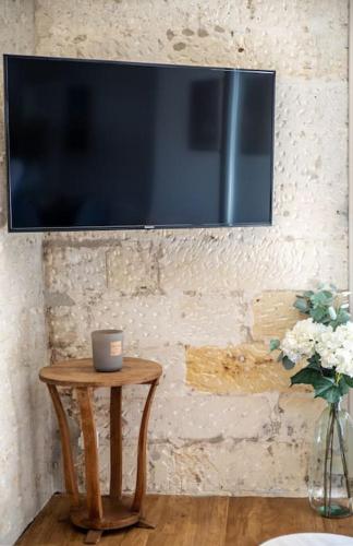 a television on a wall with a table and a vase of flowers at Sublime T2 avec balcon, wifi, linge #centre ville in Cognac