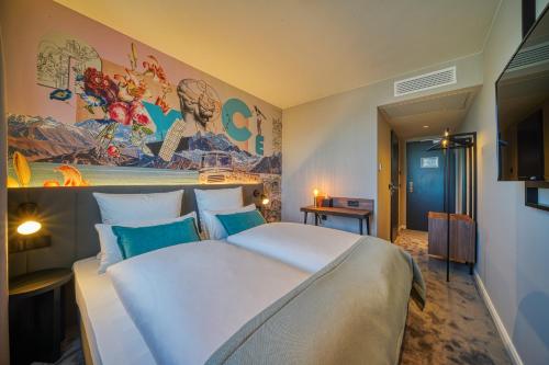 - une chambre avec un grand lit blanc orné d'une peinture murale dans l'établissement NYCE Hotel Ulm, à Ulm
