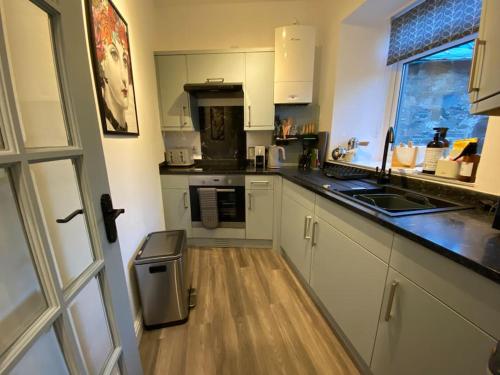 a kitchen with white cabinets and a wooden floor at The Wee Bunk House - Innerleithen in Innerleithen